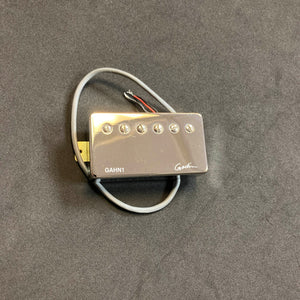 A Godin Neck Humbucker pickup with a nickel cover (model GAHN1), featuring attached wires and designed to enhance sound, is placed on a black surface.