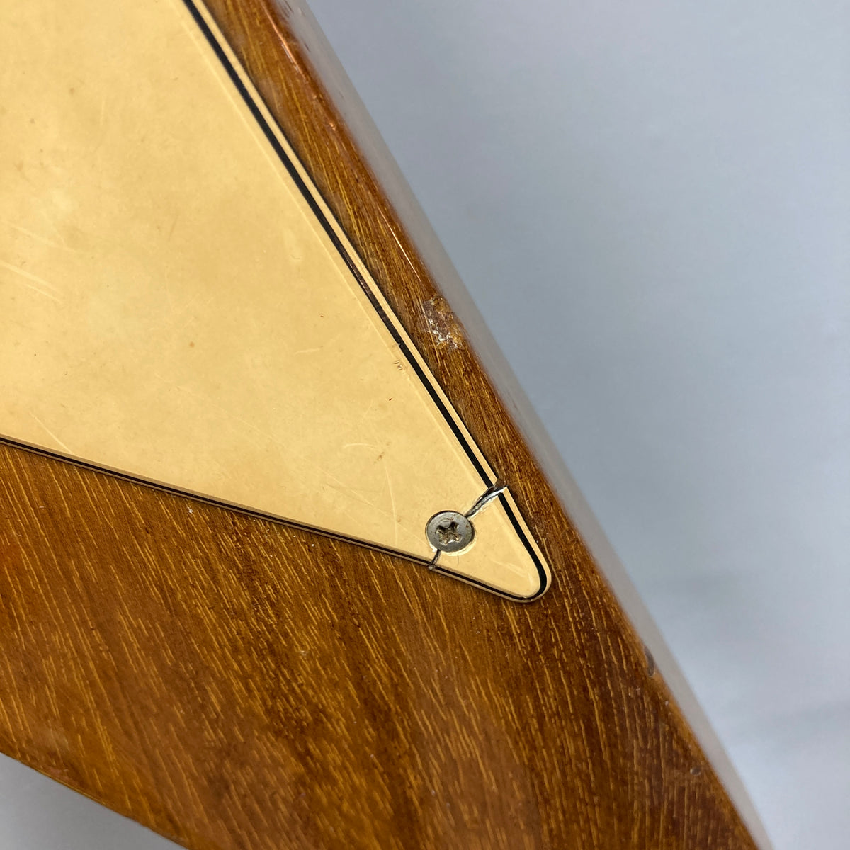 Close-up of the 1975 Gibson Flying V w/Case by Gibson, featuring a wooden body with a triangular yellow plate fastened by a single screw, displaying surface scratches and wear that highlight its natural vintage finish.