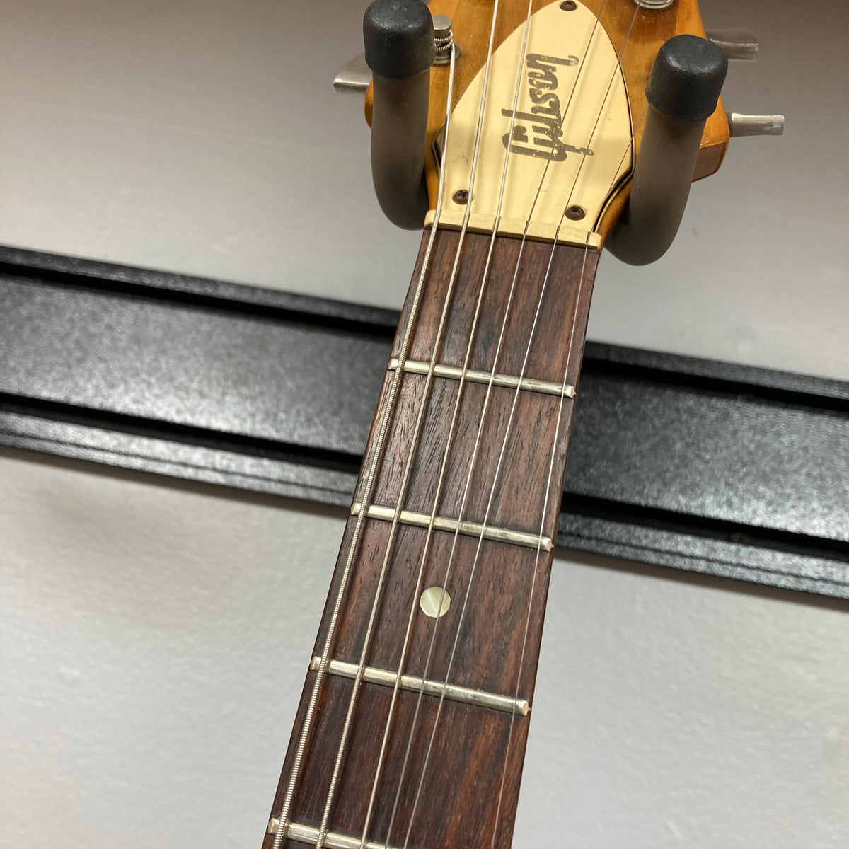 Close-up of the headstock of a 1975 Gibson Flying V w/Case by Gibson, showing part of the fretboard with six strings and a wall-mounted guitar hanger, featuring the iconic vintage Flying V design with a natural finish.