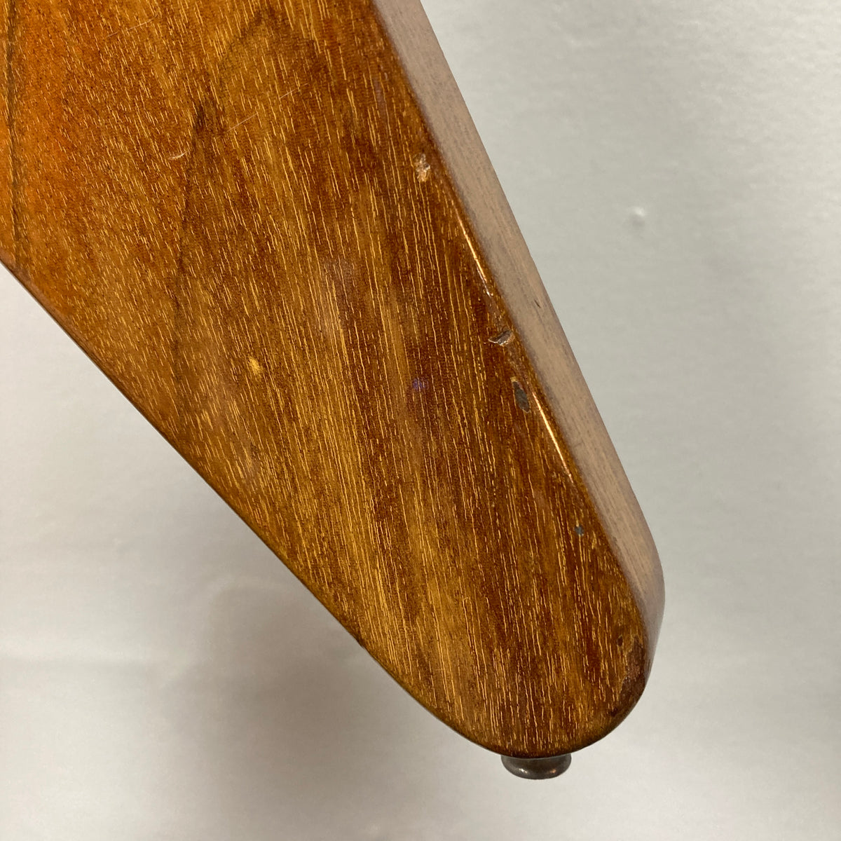 Close-up of a 1975 Gibson Flying V by Gibson with a glossy natural finish, showing some scratches and featuring a small round knob at the bottom, reminiscent of a vintage Flying V guitar, against a plain white background.