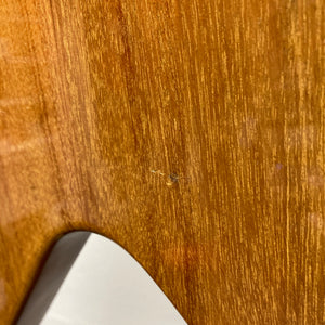 Close-up of a wooden surface with a small scratch near the center, reminiscent of the natural finish on the Gibson 1975 Flying V w/Case. A white object is partially visible in the lower left corner.