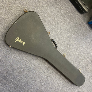 A black, hard-shell Gibson case featuring a gold Gibson logo—designed to fit the 1975 Gibson Flying V w/Case or other vintage Flying V models—is lying closed on a gray carpeted floor.