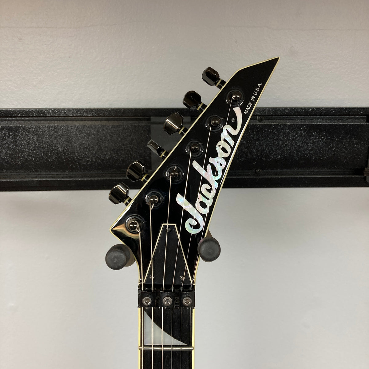 Close-up of the headstock of a black 1995 Jackson SL1 Soloist Custom Shop Eerie Dess Swirl electric guitar, featuring six tuning pegs, the Jackson logo, and “Made in U.S.A.” text, mounted on a wall hanger against a white background.