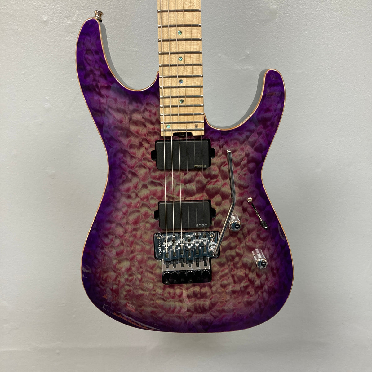The 2019 ESP USA M-II Purple Haze Burst w/Case, crafted in the USA by ESP, features a stunning quilted maple top in Purple Haze Burst, two black humbucker pickups, a maple fretboard, and a Floyd Rose tremolo bridge—photographed here against a plain light gray wall.