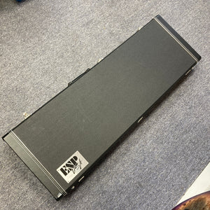 A black rectangular hard case with a handle, featuring a “Lynx USA” label, rests on a gray carpeted floor—perfect for safely storing your ESP 2019 USA M-II Purple Haze Burst electric guitar or proudly presenting this exceptional American-made ESP model.