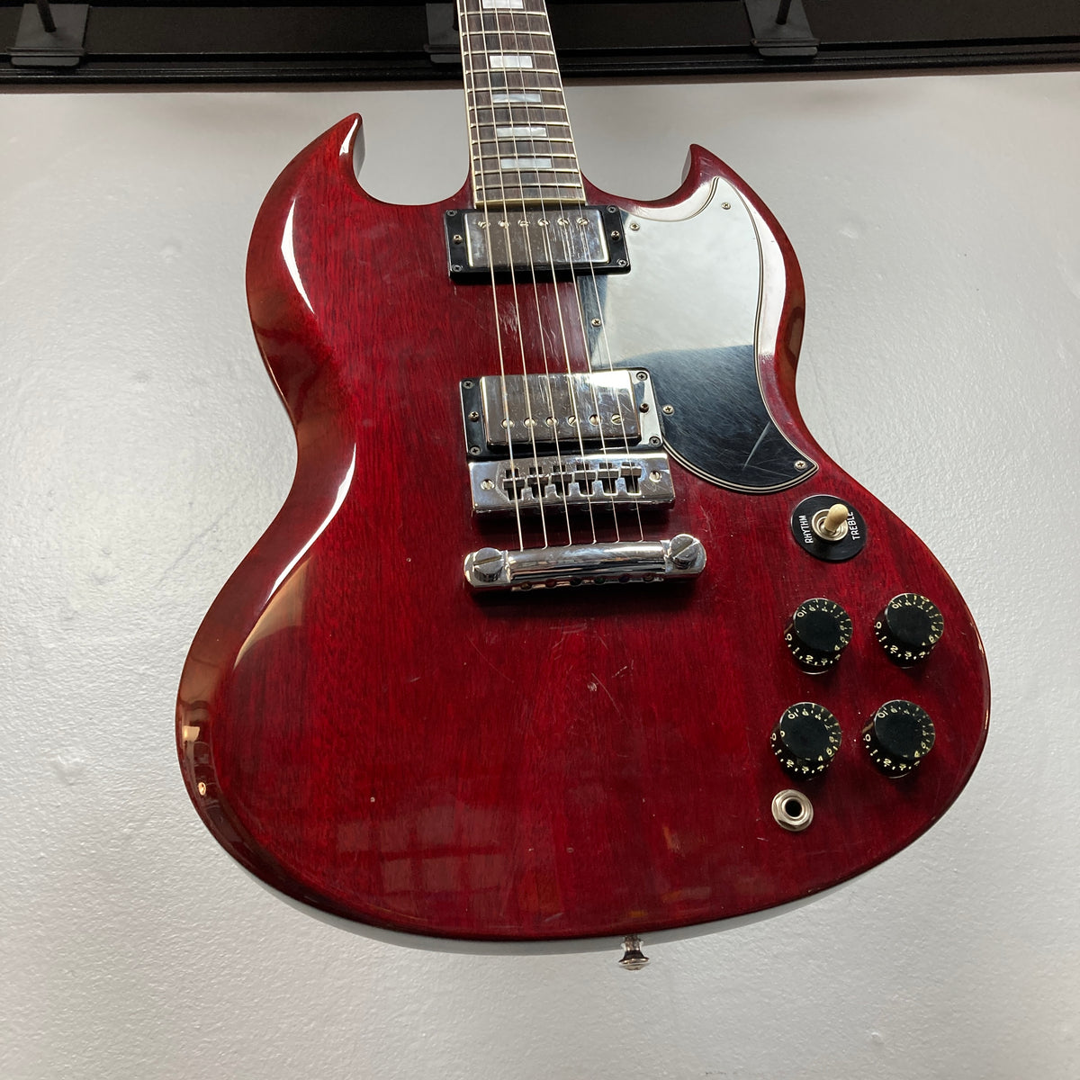 Displayed against a light background is the 1977 Gibson SG Standard Cherry w/Case by Gibson—a red electric guitar featuring a glossy finish, black pickguard, two humbucker pickups, four control knobs, and a three-way switch. With its classic mahogany body inspired by the acclaimed Gibson Kalamazoo era, this instrument seamlessly blends vintage style with timeless tone.