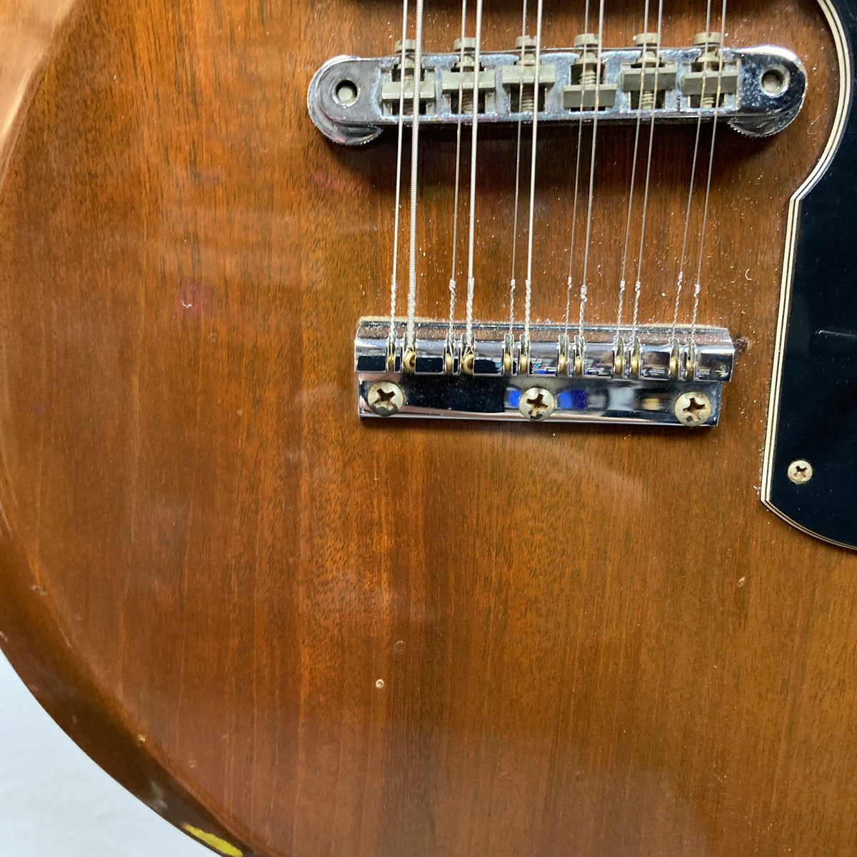 Close-up of a brown electric guitar body showing the bridge, part of the pickups, strings, and pickguard, evocative of the iconic double-neck design introduced by Gibson’s 1978 EDS-1275 Double Neck Walnut.