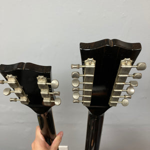 Two guitar headstocks with tuning pegs, one on the left and one on the right, are shown against a light gray wall. A hand holds the left guitar neck, which appears to be from a Gibson 1978 EDS-1275 Double Neck Walnut w/Case.