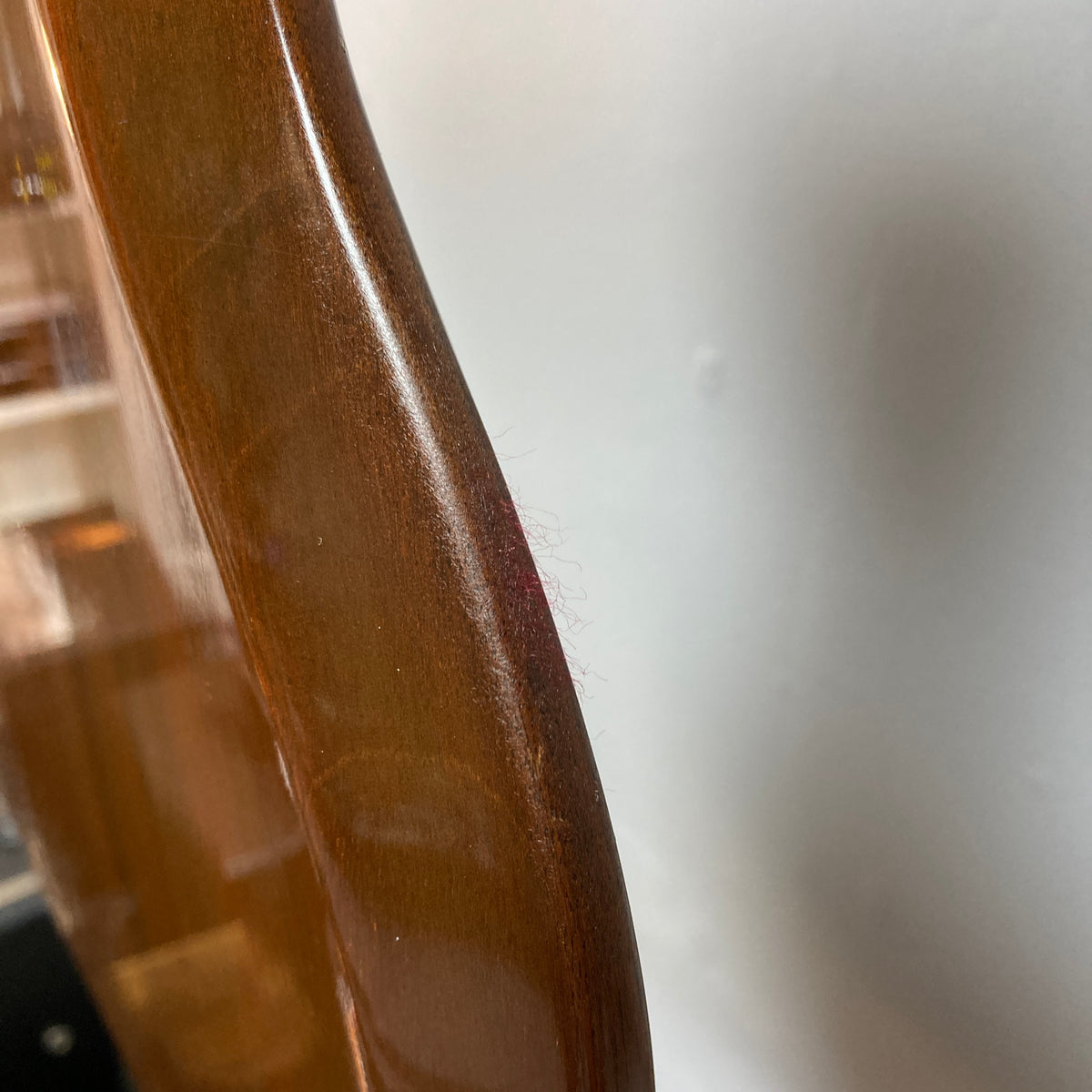 Close-up of a wooden chair leg with some fine pink fibers or threads caught on its edge, set against a blurred indoor background and a white wall—reminiscent of the subtle textures found on the finish of a classic Gibson 1978 EDS-1275 Double Neck Walnut w/Case.