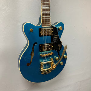 A Gretsch G2655TG Streamliner Riviera Blue Refurb semi-hollow electric guitar with gold hardware, Broad’Tron BT 3S pickups, a Bigsby tremolo, and an f-hole is hanging on a white wall.