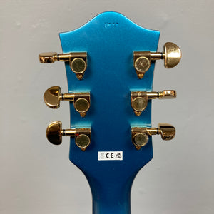 Back of a Riviera Blue Gretsch G2655TG Streamliner Refurb semi-hollow electric guitar headstock featuring six gold tuning pegs and a white sticker with certification symbols.