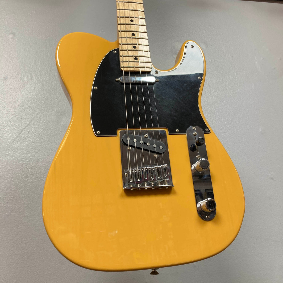Fender Player Telecaster 75th Anniversary Butterscotch Used electric guitar by Fender, featuring a black pickguard, maple fingerboard, and chrome hardware, displayed against a plain light gray wall.