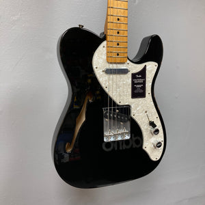 A Fender Vintera II ’60s Telecaster Thinline Black Used electric guitar by Fender, featuring a white pearl pickguard, maple neck, vintage-style Tele pickups, and an f-hole, graces the wall. Its semi-hollow ash body enhances both its classic appearance and resonant tone.