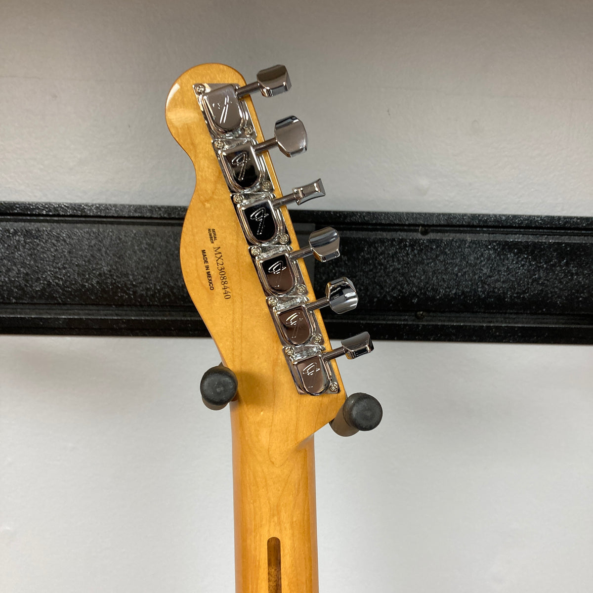 The back of a guitar headstock showing six tuning pegs and part of a black wall-mounted guitar holder, belonging to a Fender Vintera II ’60s Telecaster Thinline Black Used by Fender.