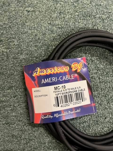 A coiled black American DJ MC-10 10ft XLR Microphone Cable lies on a textured green surface, with a label indicating "Female XLR to Male XLR.