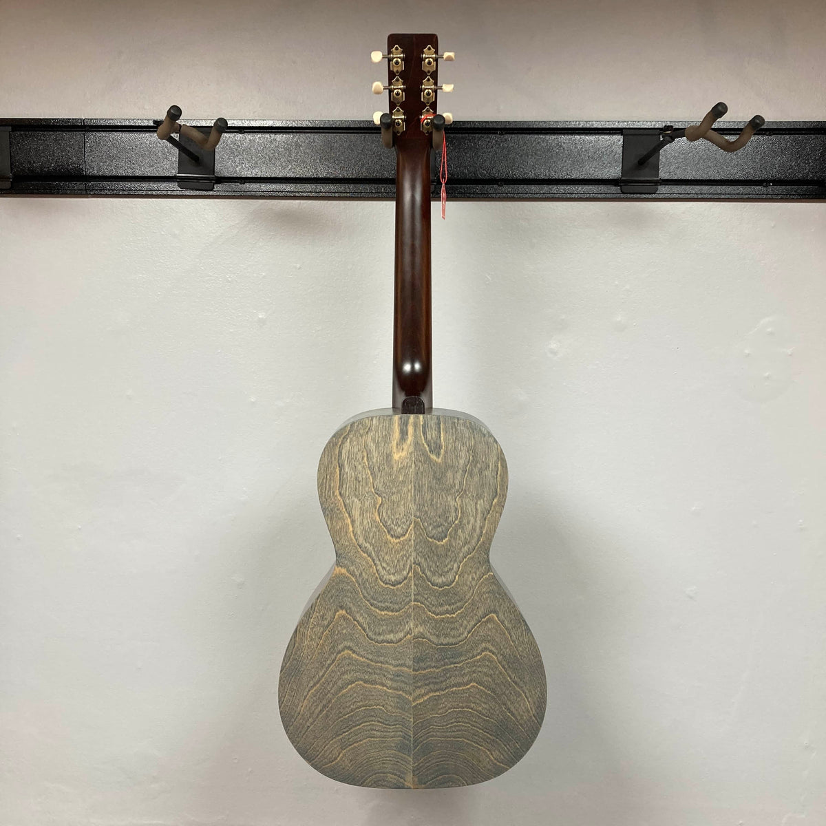 An Art & Lutherie Roadhouse Denim Blue Q-Discrete acoustic guitar hangs by its neck on a black wall-mounted rack against a white wall.