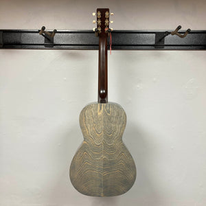 An Art & Lutherie Roadhouse Denim Blue Q-Discrete acoustic guitar hangs by its neck on a black wall-mounted rack against a white wall.