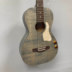The Art & Lutherie Roadhouse Denim Blue Q-Discrete acoustic guitar features a denim blue finish and white pickguard, with six strings and two amber control knobs, displayed against a light gray wall.