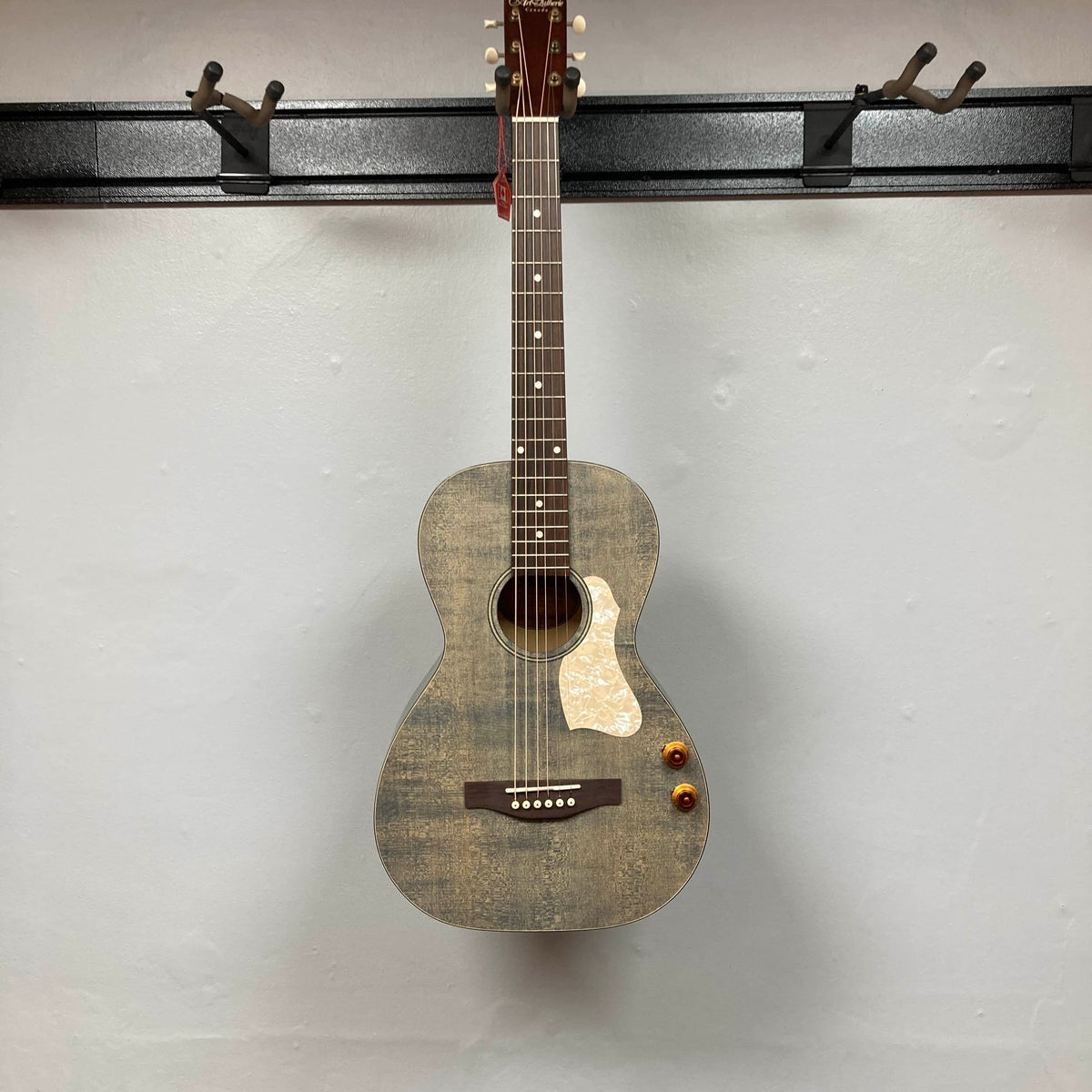An Art & Lutherie Roadhouse Denim Blue Q-Discrete acoustic guitar hangs on a wall-mounted rack against a plain white background.