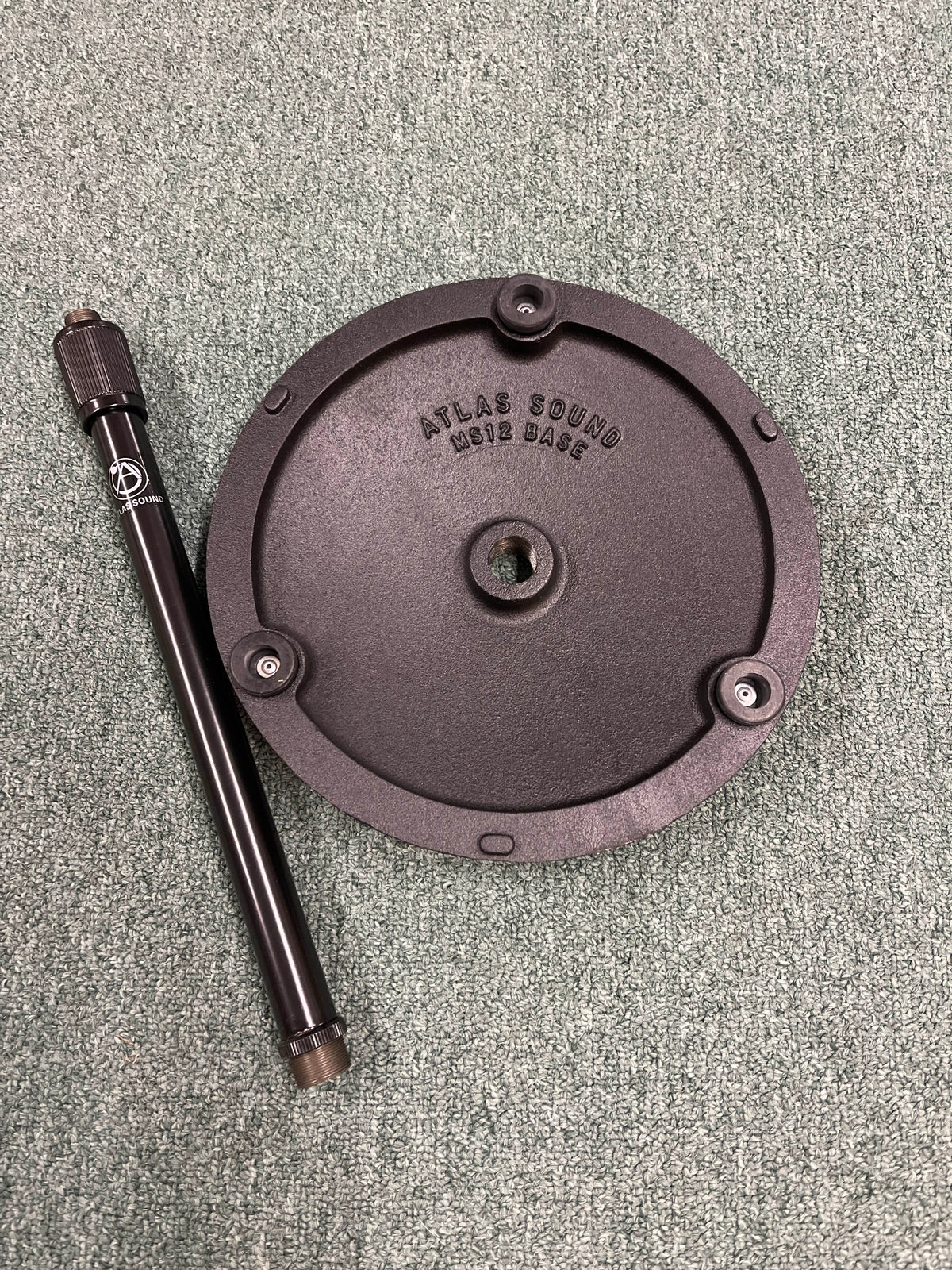 An Atlas Sound DMS10E Mic Stand Base with Extension Rod sits on a textured green surface.