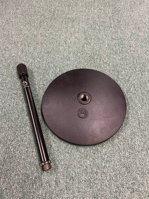 An Atlas Sound DMS10E Mic Stand Base with Extension Rod, both in black and featuring the brand’s logo, are set on a textured green surface.