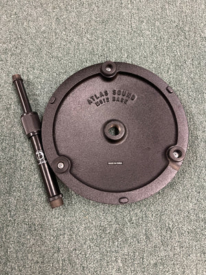 The Atlas Sound DMS7E Mic Stand Base with Extension Rod is shown in black, featuring a round base with three screws and a detachable rod, all placed on a textured green carpet.