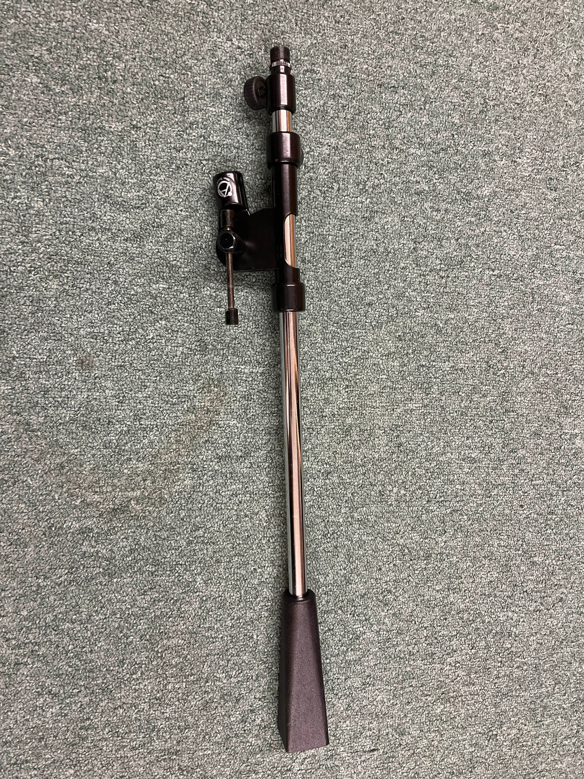 An Atlas Sound PB21XCH Professional Microphone Stand Boom by Atlas Sound rests on a speckled gray carpeted floor, its sleek design reminiscent of studio recording or live sound equipment.