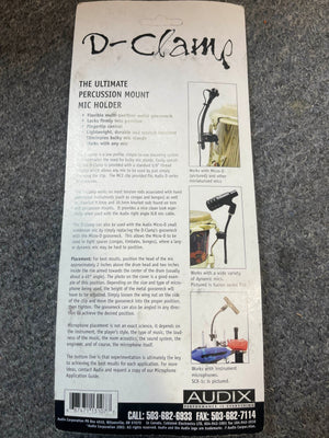 Back of an Audix D-Clamp Percussion Mount Mic Holder package by Audix, showing features, mounting instructions, compatibility details, and contact info on a gray carpet background.
