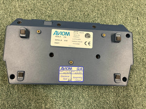 The underside of an Aviom AN-16/II A-Net Input Module shows model and serial number labels, certification marks, and quality assurance stickers on a green carpet.