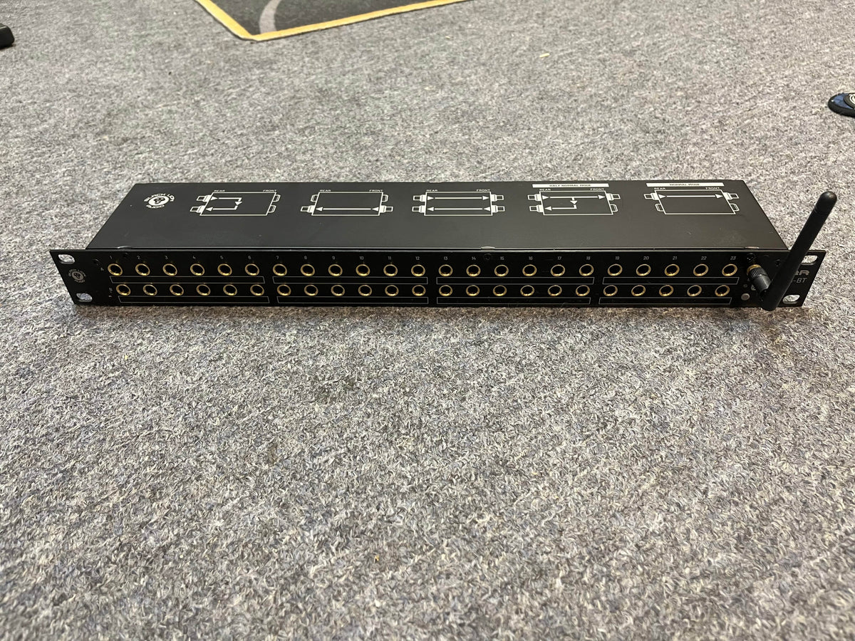 A Black Lion Audio PBR TRS-BT 46-point gold-plated TRS patchbay with Bluetooth (1 RU) and a small antenna is on a grey carpeted floor, featuring multiple rows of input and output jacks.