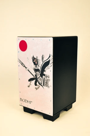 The Bodhi Cajon Drum - Art Collection #3 by Bodhi is a black rectangular cajon with short legs, a white panel featuring a stylized figure, a red circle in the top left, and "BODHI" at the bottom—a perfect art piece for music lovers.