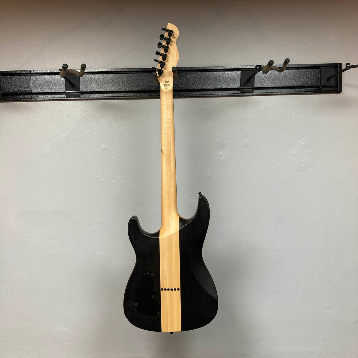 A Chapman ML1 Pro Modern Lunar electric guitar with 24 frets is displayed on a wall-mounted rack, shown from the back with its neck and headstock visible.