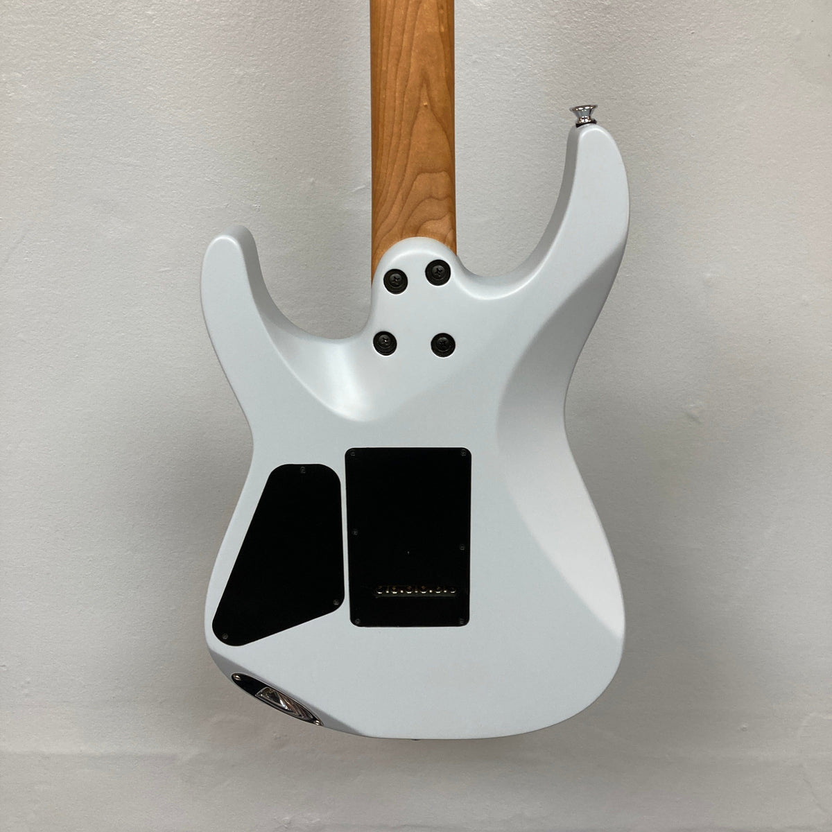 The image shows the back of a used Charvel DK24 HSS 2PT CM Electric Guitar in gray, featuring a natural wood neck, two black rectangular cover plates with four screws near the neck joint, set against an off-white wall.
