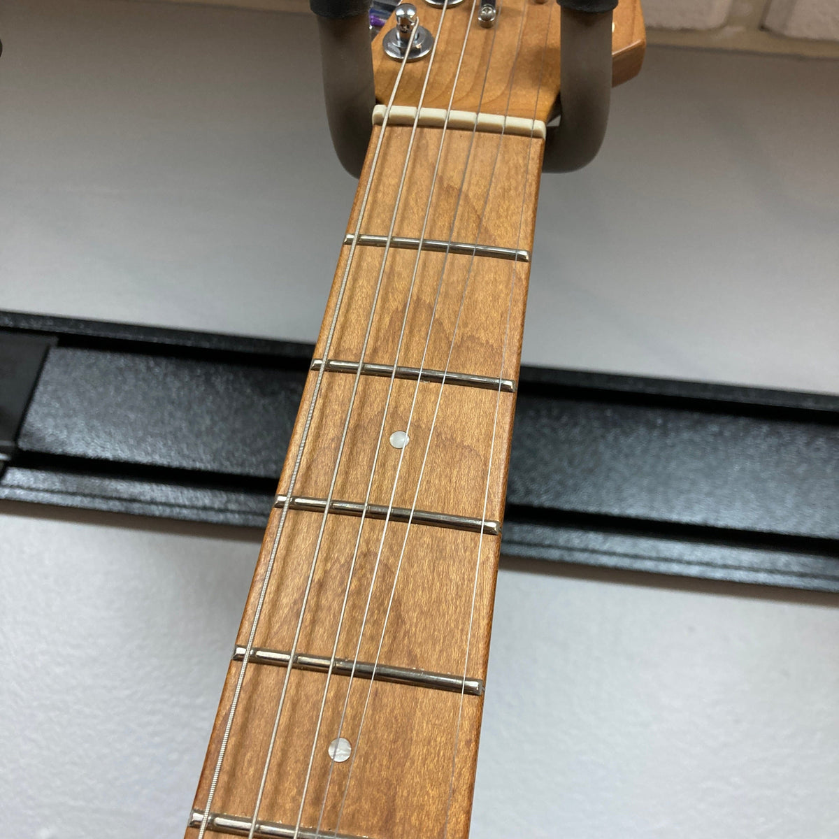 A close-up of the Charvel DK24 HSS 2PT CM Electric Guitar - Gray shows its neck, six strings, metal frets, and two dot inlays. This used Charvel guitar is wall-mounted against a light-colored background.