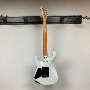 A Used Charvel DK24 HSS 2PT CM Electric Guitar - Gray by Charvel hangs by its neck on a wall-mounted metal rack. The back view shows the wooden neck and black access panels against a plain white wall.