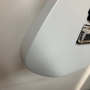 Close-up of the bottom edge of a gray Used Charvel DK24 HSS 2PT CM Electric Guitar body against a white wall, with chrome bridge hardware partially visible on the right.