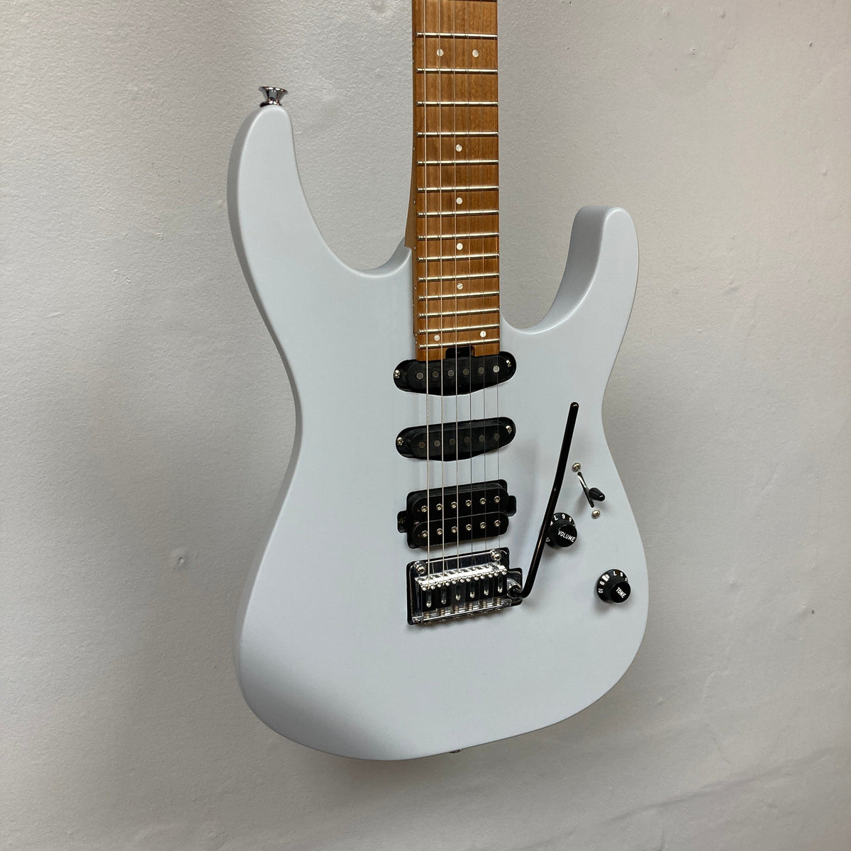 A gray Charvel DK24 HSS 2PT CM electric guitar by Charvel, featuring black pickups, a whammy bar, and two control knobs, shown against a plain white wall.