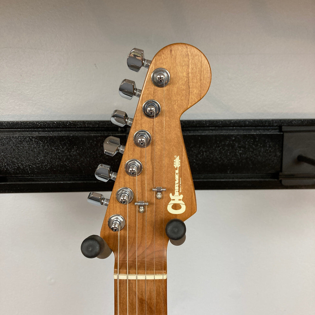 A close-up of the Charvel DK24 HSS 2PT CM Electric Guitar headstock, showing six tuning pegs, strings, and the Charvel logo. The used gray guitar is mounted on a wall hanger against a plain white background.