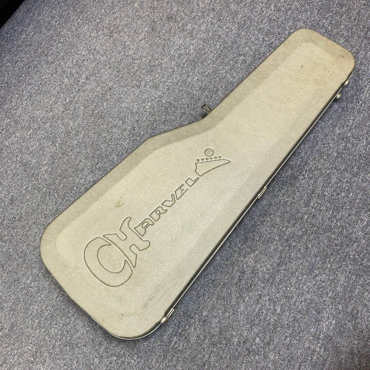 A Charvel Model 4 HSS Red electric guitar, complete with its original hard shell case, rests closed on a gray carpeted floor, showcasing the classic Charvel style.