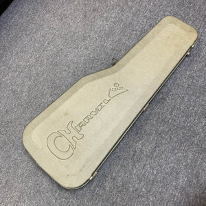 A Charvel Model 4 HSS Red electric guitar, complete with its original hard shell case, rests closed on a gray carpeted floor, showcasing the classic Charvel style.