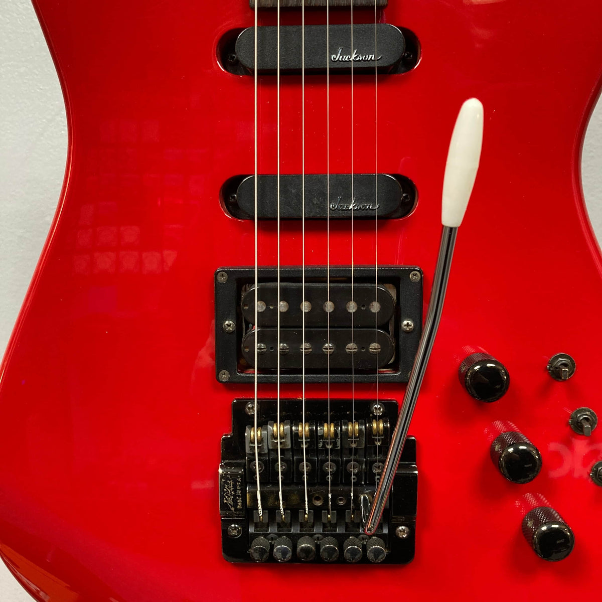 Close-up of a red Charvel Model 4 HSS electric guitar, featuring three pickups, whammy bar, control knobs, and bridge—an iconic design by Charvel.