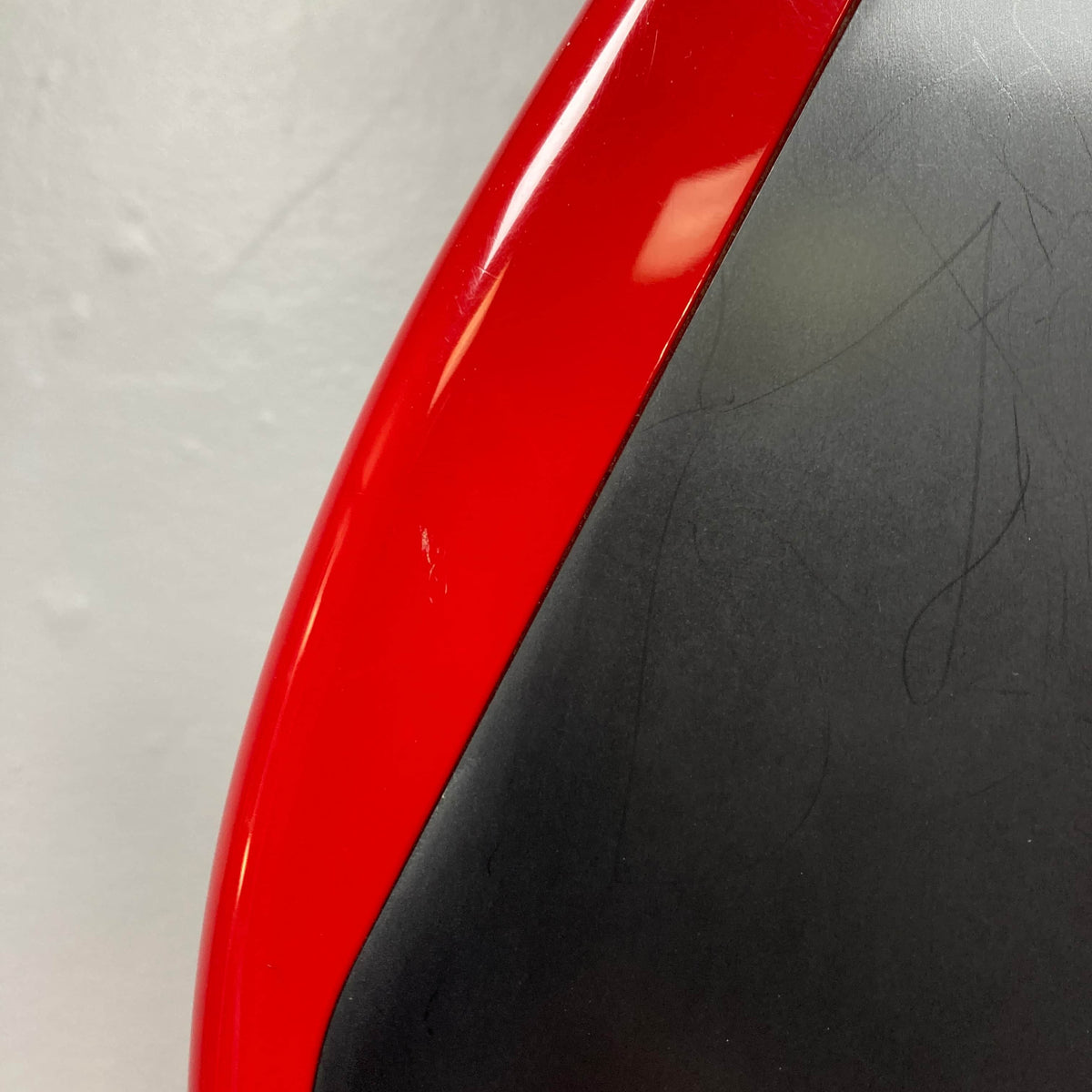 Close-up of a Charvel Model 4 HSS Red w/OHSC Consign electric guitar with curved edges, its black surface showing signs of wear, set against a light gray background—highlighting the vintage character and classic HSS setup.