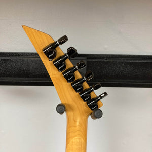 Back of a Charvel Model 4 HSS Red headstock with six black tuners on natural wood, hanging on a wall mount.