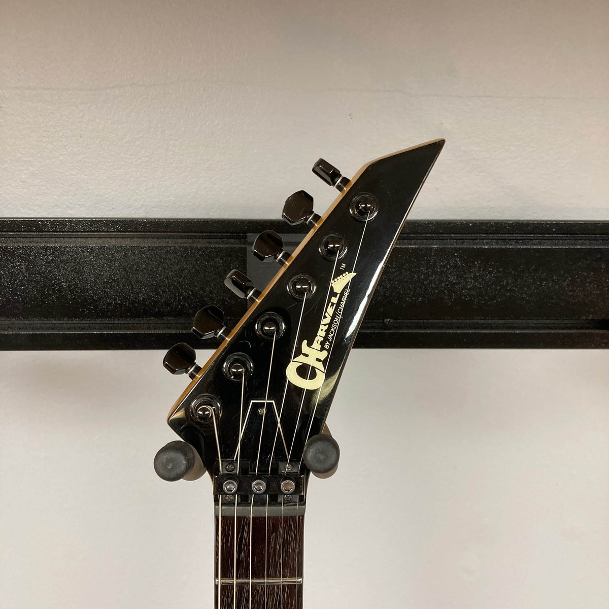 Close-up of the headstock of a Charvel Model 4 HSS Red w/OHSC Consign electric guitar by Charvel, featuring black tuning pegs and visible logo against a plain background.
