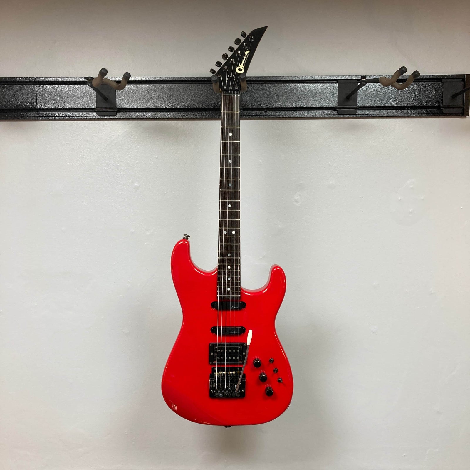 The Charvel Model 4 HSS Red electric guitar by Charvel features a black pickguard, three pickups, five control knobs, and a tremolo bridge, and is shown against a plain white wall. Comes with original hard shell case. The Charvel Model 4 HSS Red electric guitar by Charvel features a black pickguard, three pickups, five control knobs, and a tremolo bridge, and is shown against a plain white wall. Comes with original hard shell case.