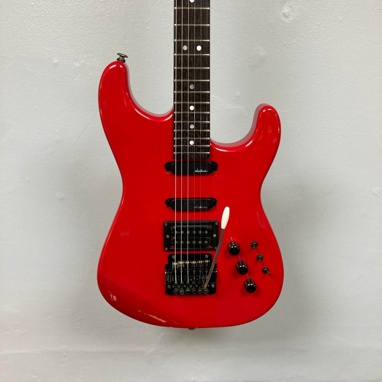 The Charvel Model 4 HSS Red electric guitar by Charvel features a black pickguard, three pickups, five control knobs, and a tremolo bridge, and is shown against a plain white wall. Comes with original hard shell case. The Charvel Model 4 HSS Red electric guitar by Charvel features a black pickguard, three pickups, five control knobs, and a tremolo bridge, and is shown against a plain white wall. Comes with original hard shell case.