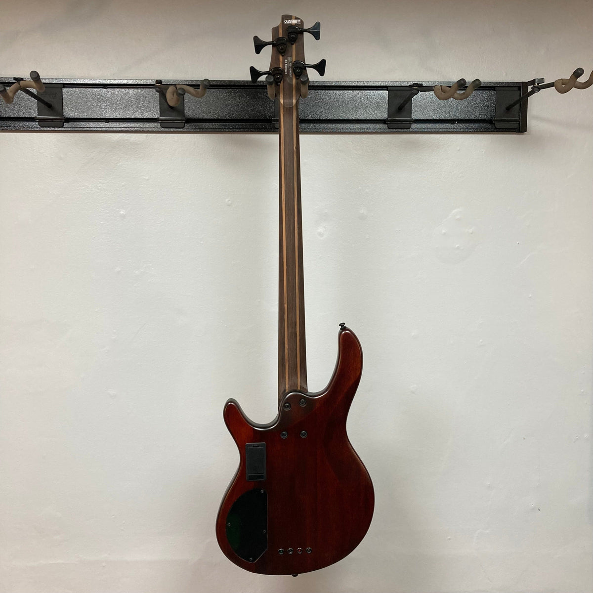 Cort Artisan B4 Element Burgundy Red bass guitar mounted on a wall, showcasing its ergonomic mahogany body and high-mass MetalCraft M4 bridge.