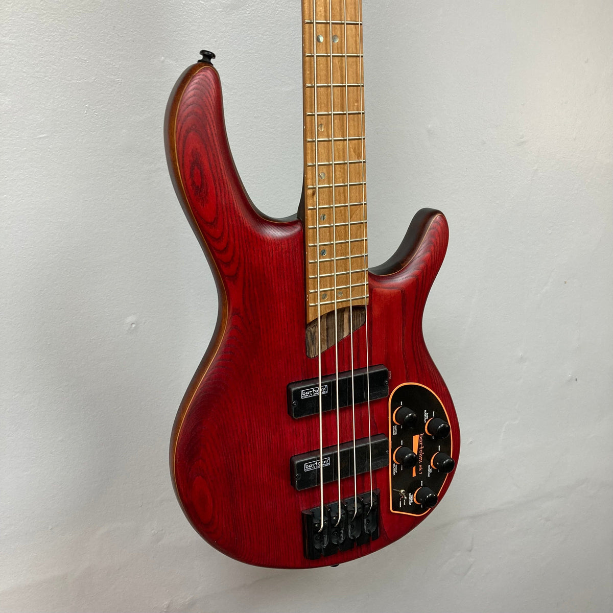 Cort Artisan B4 Element Burgundy Red electric bass guitar displayed on a wall, highlighting its craftsmanship and high-quality components.