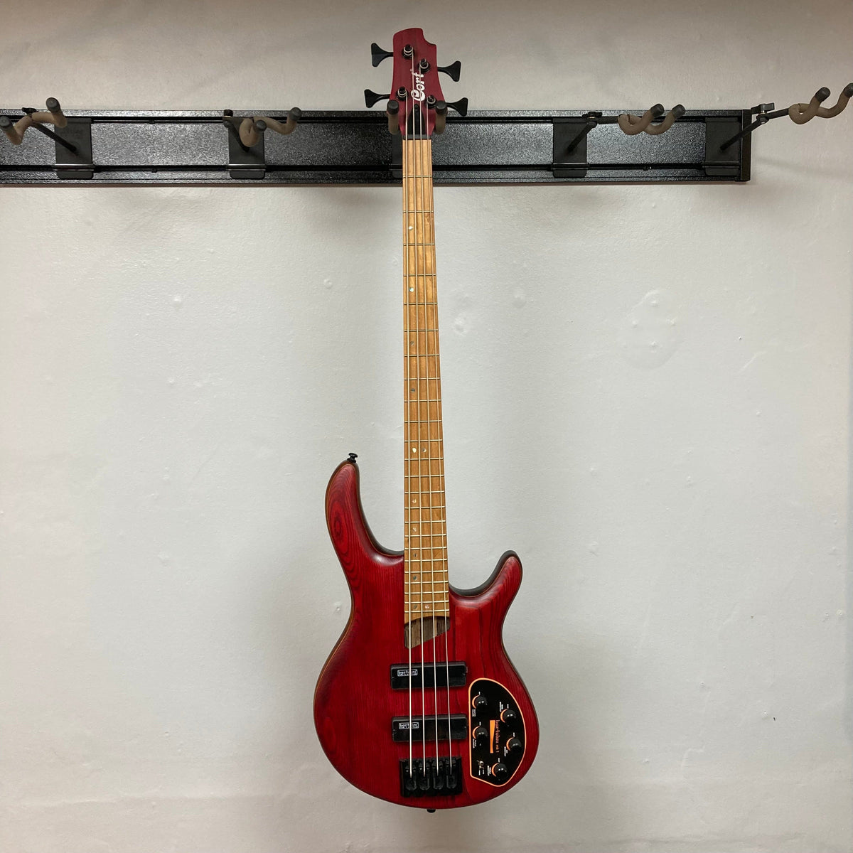 Cort Artisan B4 Element Burgundy Red bass guitar hanging on a hook, showcasing its ergonomic design and high-mass MetalCraft M4 bridge.