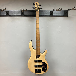 Cort Artisan B4 Element Natural bass guitar with a roasted maple fretboard, Bartolini® MK-1 pickups, and a MetalCraft M4 bridge, displayed on a wall.